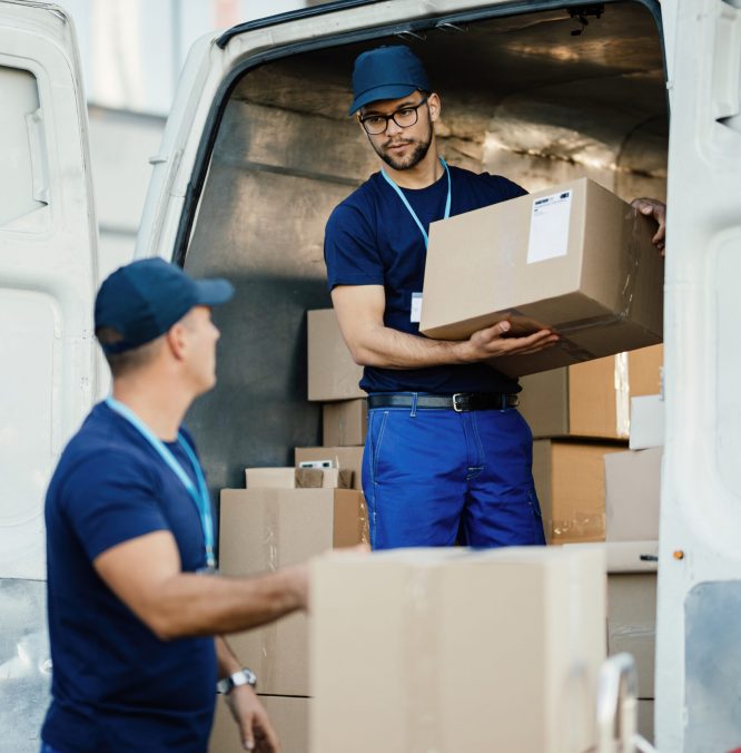 Young worker loading cardboard boxes in a delivery van and communicating with his colleague.