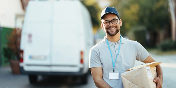 Portrait of happy delivery man carrying packages and looking at camera while standing on the street.